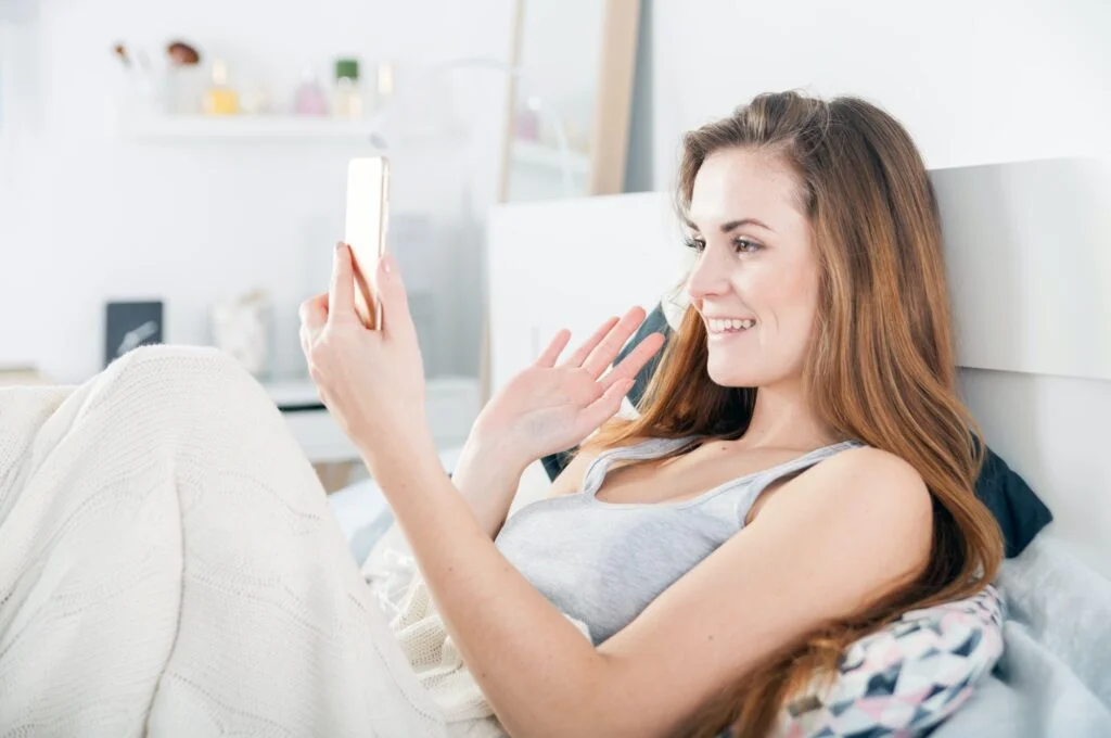 Young girl lying in bed and video calling on smart phone