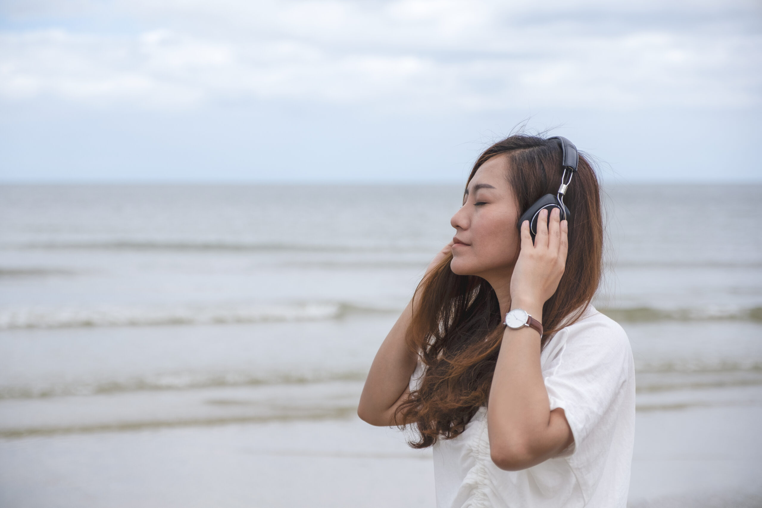 A sad woman listening to music with headphone by the sea